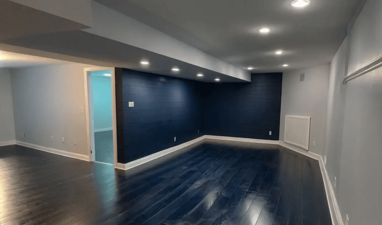 A finished basement with a deep navy feature wall and dark hardwood floor